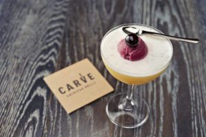 A branded Carve American Grille coaster next to a craft cocktail